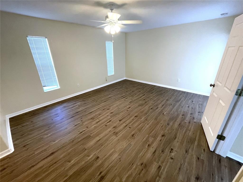 An empty bedroom features light-colored walls, wood-look flooring, two windows, and a ceiling fan — 2498 MARGARET LANE, NORTH PORT, FL