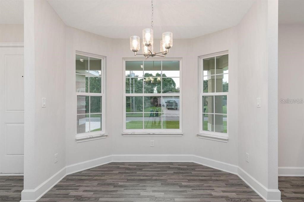 A bright dining nook features three windows, a modern chandelier, and wood-look flooring — 48 PHEASANT DRIVE, PALM COAST, FL