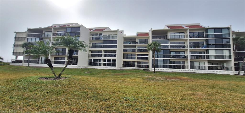 A multi-story apartment building with balconies and a red roof sits behind a grassy lawn — 7907 SAILBOAT KEY BOULEVARD S UNIT 205, SOUTH PASADENA, FL