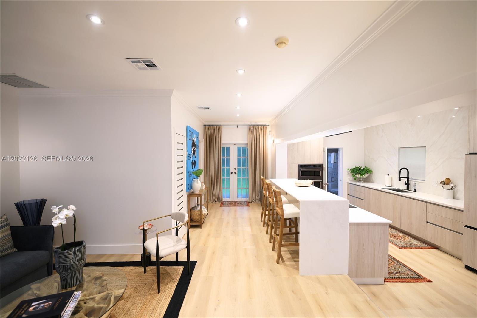A modern kitchen and living area feature light wood flooring, white cabinetry, and a waterfall island — 2338 SW 11th St # 2338, Miami FL 33135, MIAMI, FL