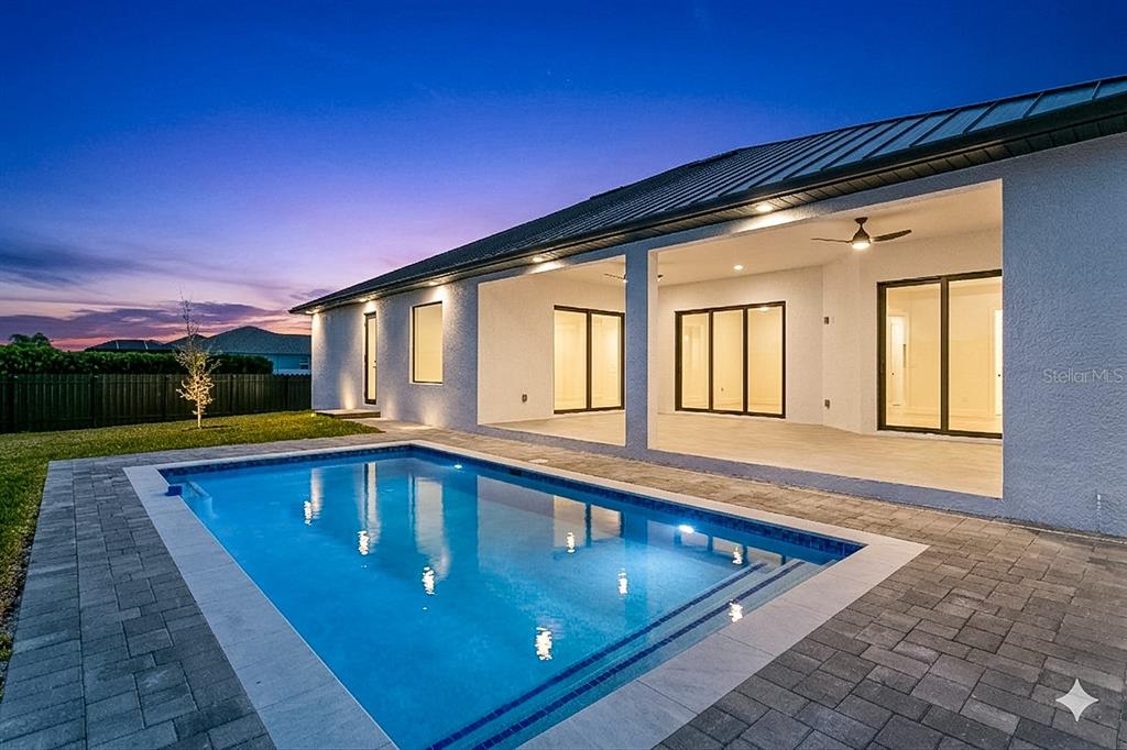 A backyard swimming pool sits in front of a house with a covered patio area — 3300 NW 1ST TERRACE, CAPE CORAL, FL