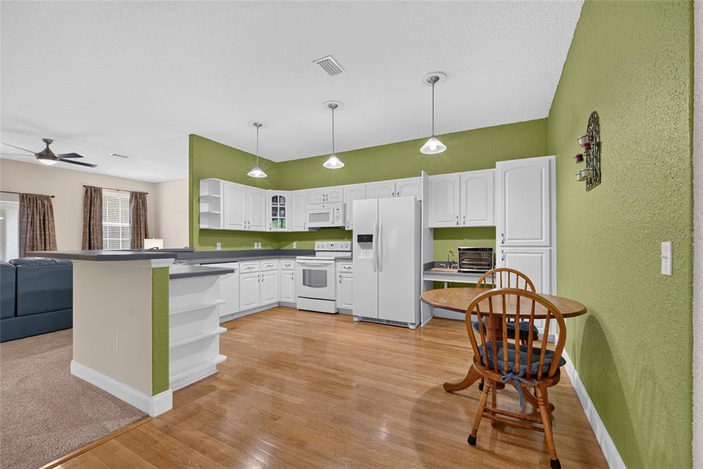 A kitchen features white cabinetry, green walls, hardwood floors, and a small wooden dining set — 3788 SE 133RD PLACE, BELLEVIEW, FL