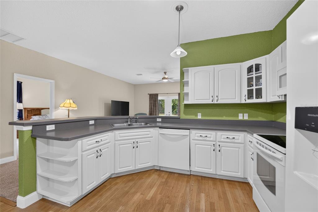 A kitchen with white cabinets, gray countertops, and hardwood floors opens to a living area — 3788 SE 133RD PLACE, BELLEVIEW, FL
