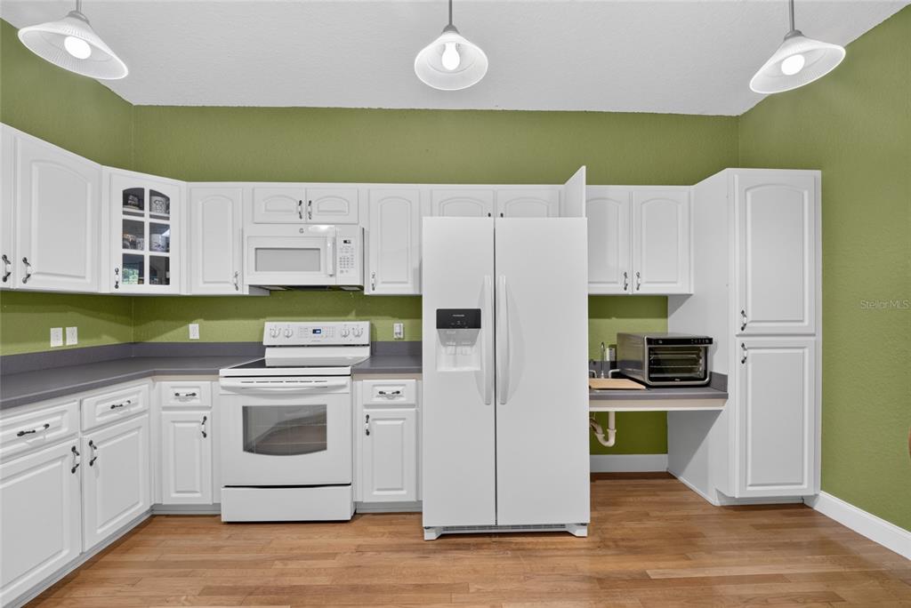 A kitchen features white cabinets, white appliances, dark countertops, and green walls — 3788 SE 133RD PLACE, BELLEVIEW, FL