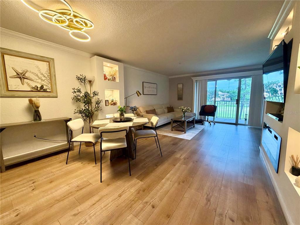 A living and dining area features light wood flooring, a modern chandelier, and a balcony view — 14049 FAIRWAY ISLAND DRIVE UNIT 124, ORLANDO, FL
