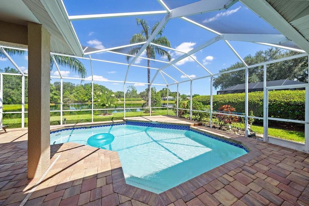 A screened-in swimming pool with a paver deck overlooks a lake and palm trees — 11909 SUMMER MEADOW DRIVE, LAKEWOOD RANCH, FL