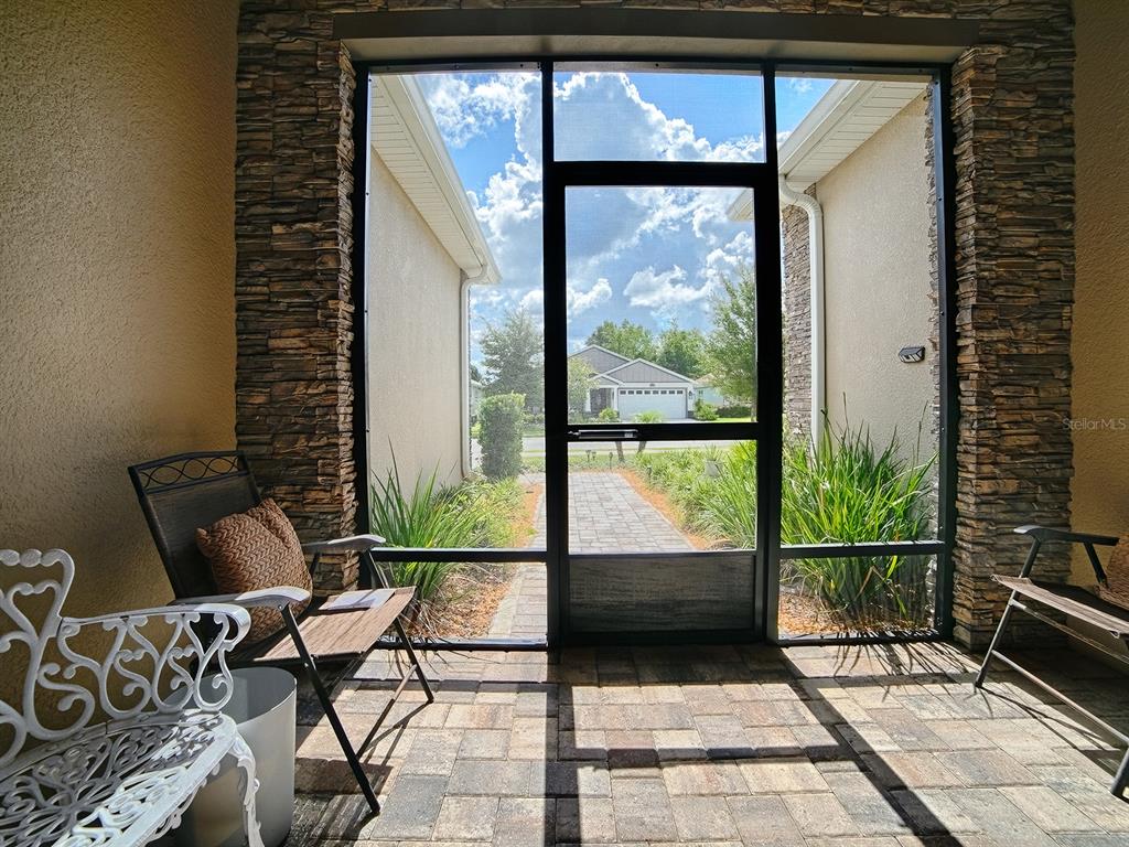 A covered patio with stone pillars, a screen door, and paver flooring overlooks a walkway — 12596 NE 49TH DRIVE, OXFORD, FL
