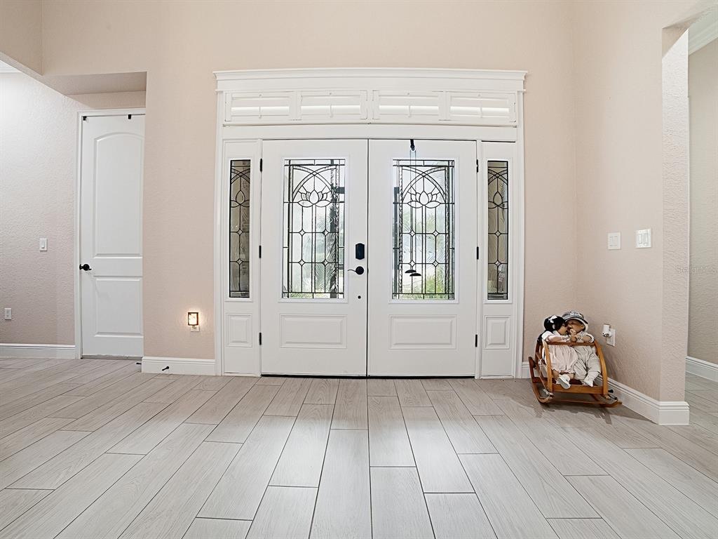 A bright entryway features light wood-look tile flooring, white double doors with glass inserts, and trim — 12596 NE 49TH DRIVE, OXFORD, FL