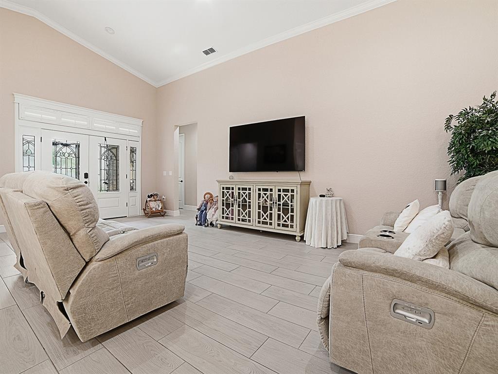 A living room features light-colored tile flooring, beige walls, a wall-mounted television, and two recliners — 12596 NE 49TH DRIVE, OXFORD, FL