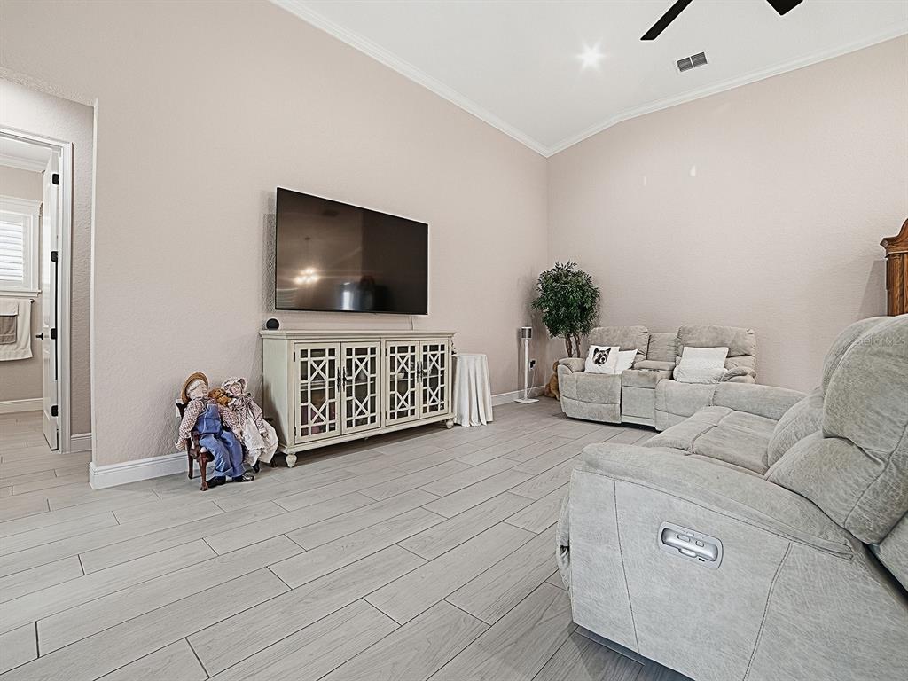 A living room features light-colored tile flooring, a wall-mounted television, and two gray reclining sofas — 12596 NE 49TH DRIVE, OXFORD, FL
