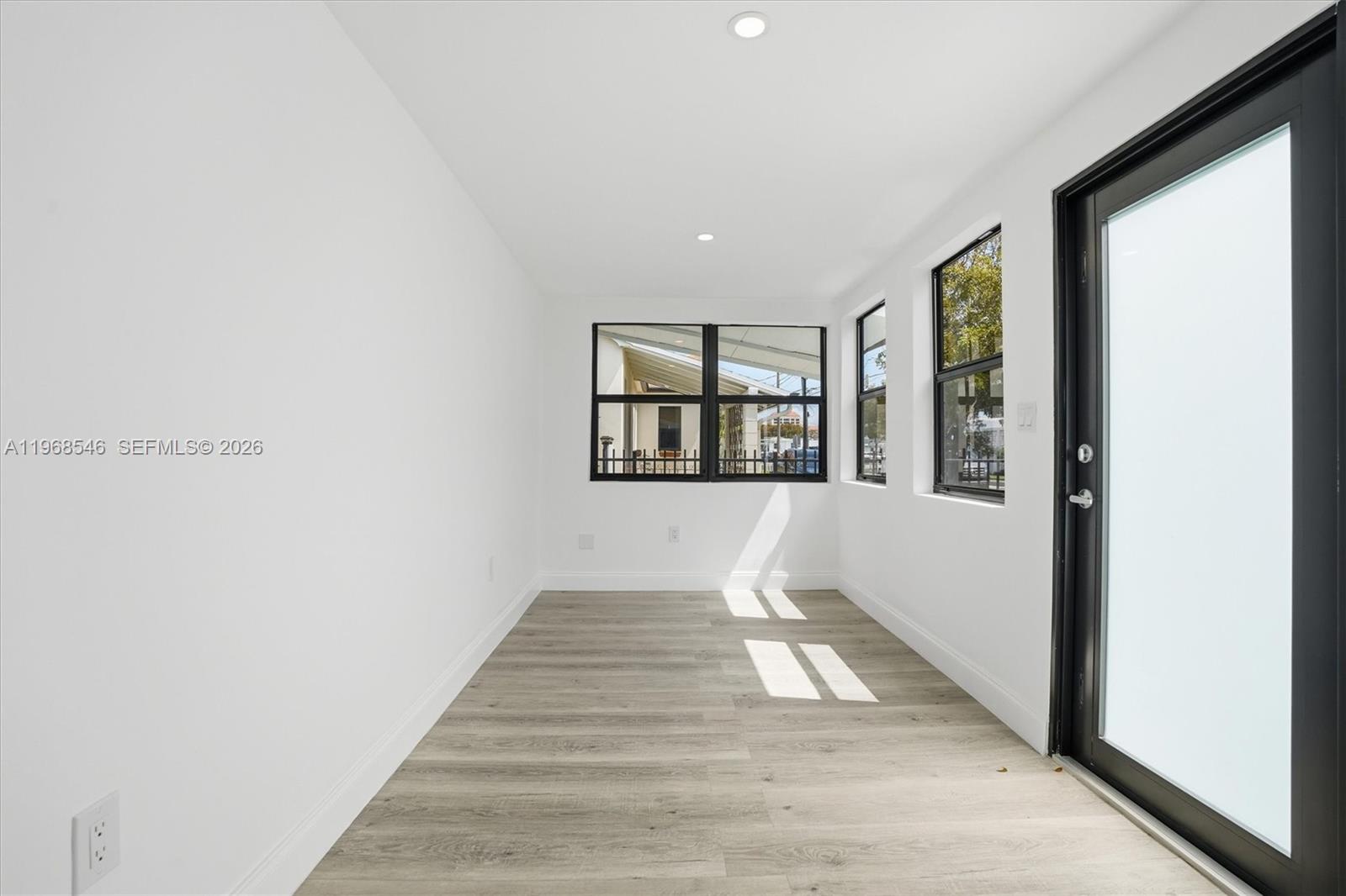 A bright, empty room features white walls, light wood-look flooring, and black-framed windows and doors — 4237 SW 7th St, Miami FL 33134, MIAMI, FL