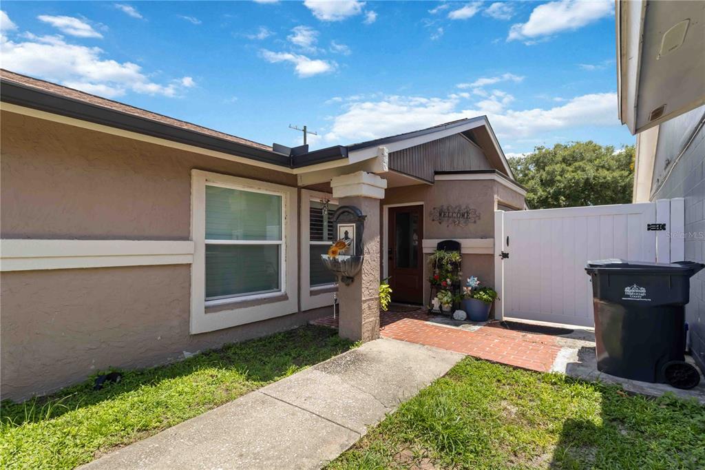 A concrete walkway leads to the front entrance of a tan house with a brick porch — 10327 PARKCREST DRIVE, TAMPA, FL