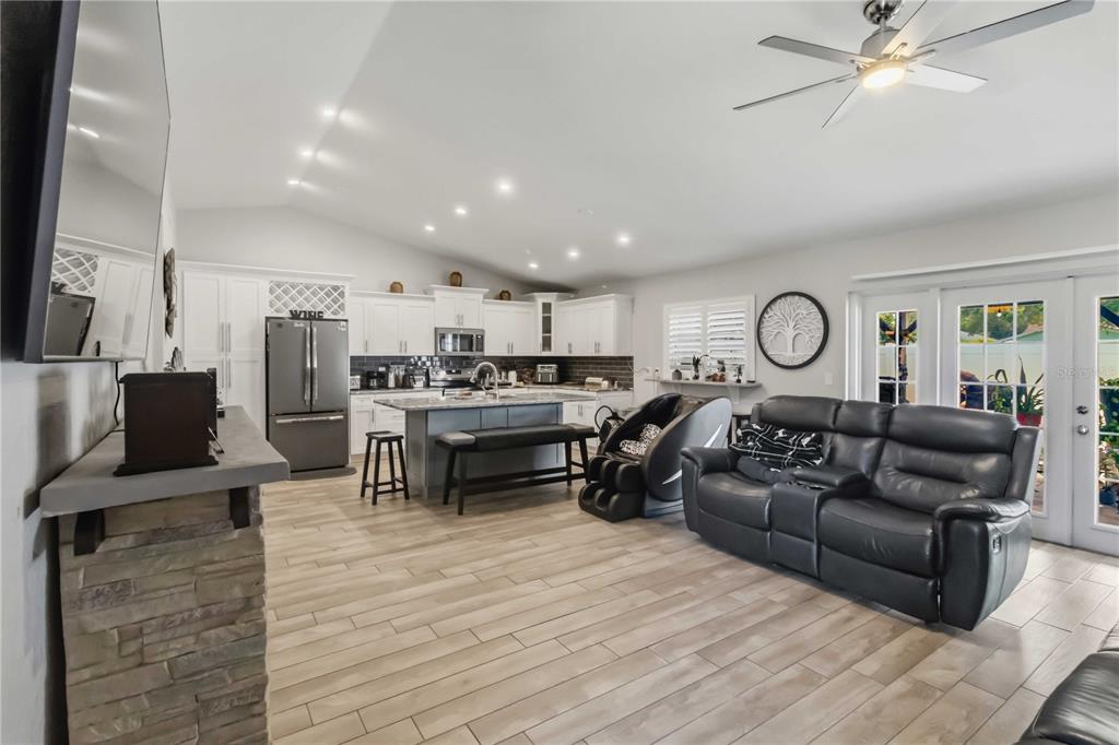 An open-concept kitchen and living area featuring white cabinetry, a stone fireplace, and wood-look flooring — 10327 PARKCREST DRIVE, TAMPA, FL