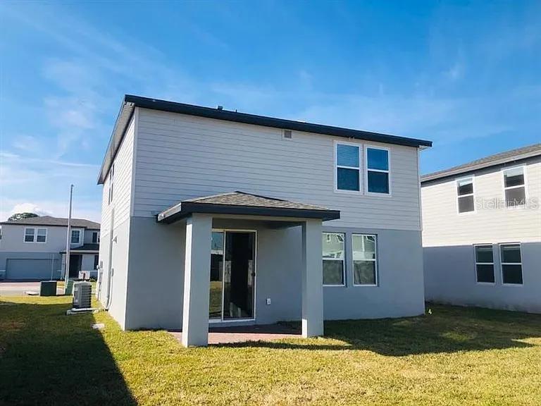 The rear exterior of a two-story house features gray siding, a covered patio, and grass — 501 SUN WARBLER WAY, ST CLOUD, FL
