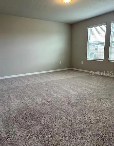 An empty bedroom features beige walls, neutral carpeting, and two windows with white blinds — 501 SUN WARBLER WAY, ST CLOUD, FL
