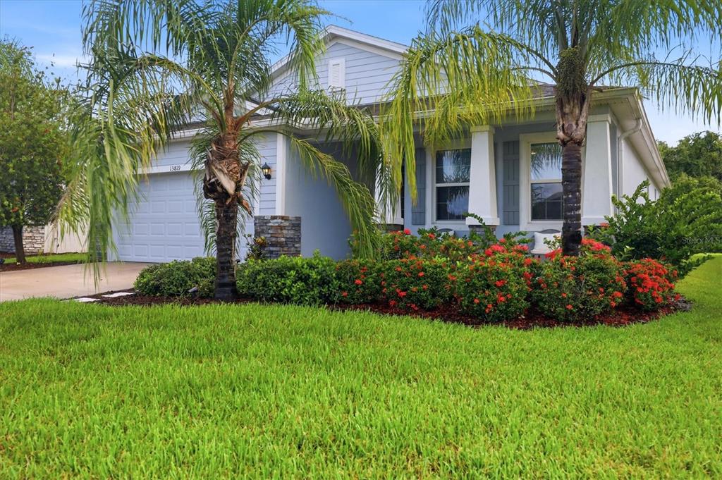 A light blue single-story house features a two-car garage, palm trees, and red flowering shrubs — 13819 CAMDEN CREST TERRACE, LAKEWOOD RANCH, FL
