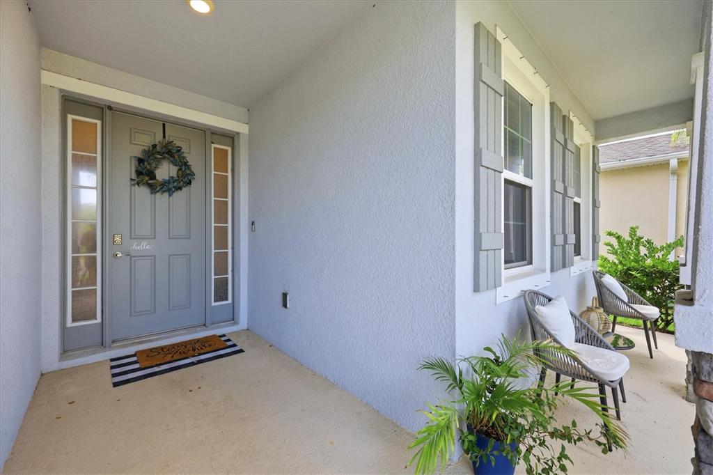 A covered front porch features a gray door with sidelights, two chairs, and a potted plant — 13819 CAMDEN CREST TERRACE, LAKEWOOD RANCH, FL