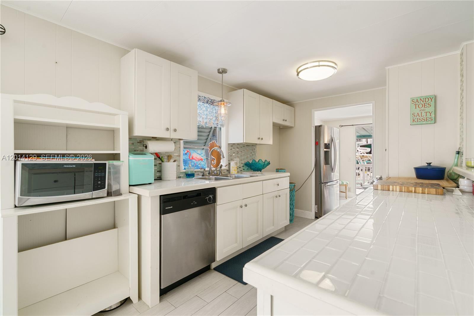 A bright kitchen features white cabinetry, a tiled countertop, stainless steel appliances, and a backsplash — 205 Humpty Dumpty Dr, Key Largo FL 33037, KEY LARGO, FL