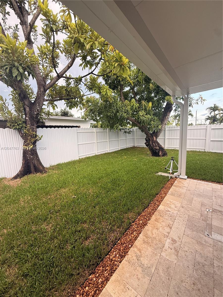 A paved patio overlooks a grassy backyard enclosed by a white vinyl fence and trees — 10555 SW 32nd St, Miami FL 33165, MIAMI, FL