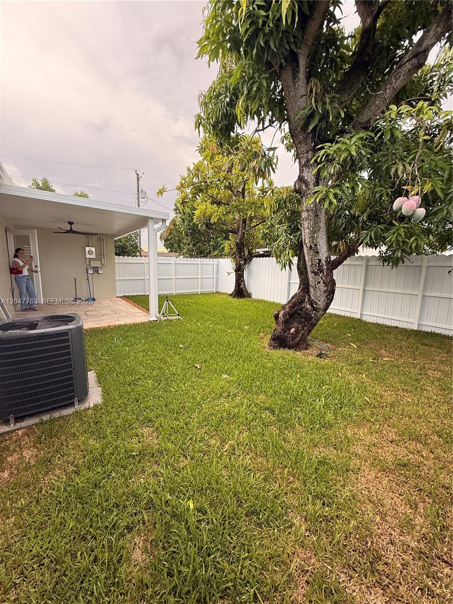 A backyard features a grassy lawn, a paved patio, a white fence, and a mango tree — 10555 SW 32nd St, Miami FL 33165, MIAMI, FL