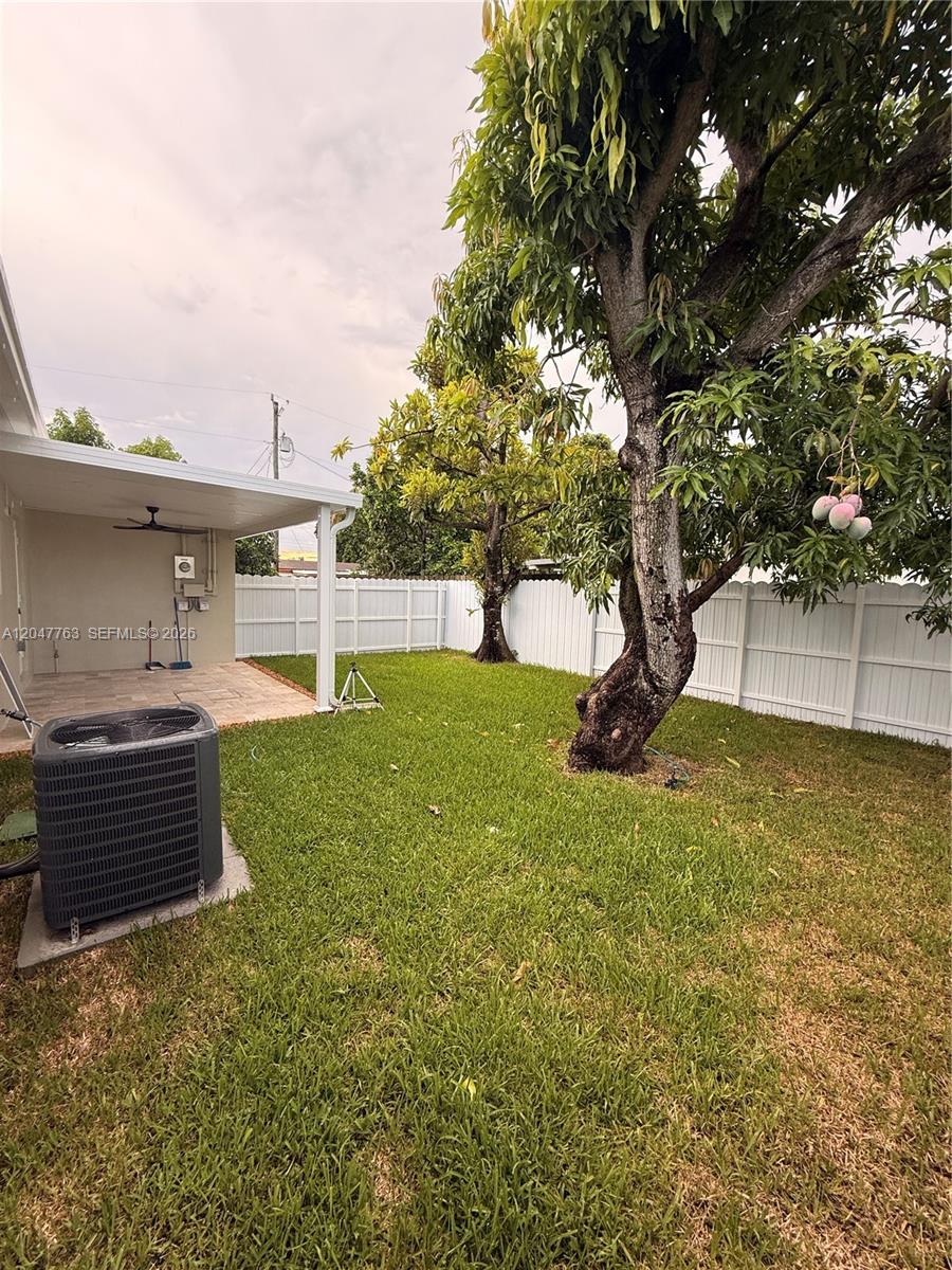 A grassy backyard features a covered patio, an air conditioning unit, and large mango trees — 10555 SW 32nd St, Miami FL 33165, MIAMI, FL