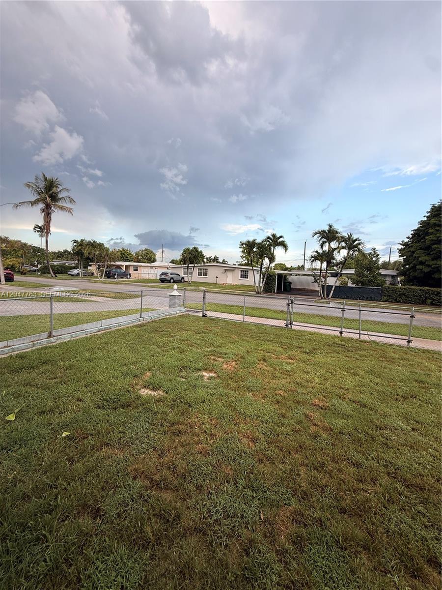 A grassy yard is enclosed by a chain-link fence with houses visible in the background — 10555 SW 32nd St, Miami FL 33165, MIAMI, FL