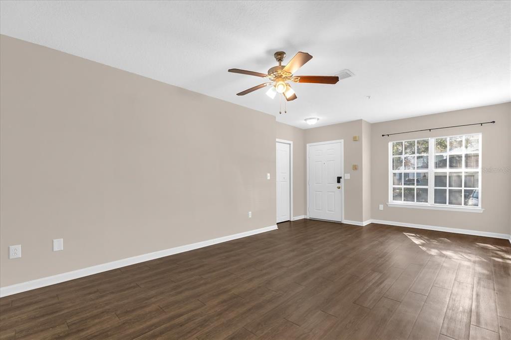 An empty living room features wood-look flooring, a ceiling fan, and a white front door — 4316 S KIRKMAN ROAD UNIT 1611, ORLANDO, FL