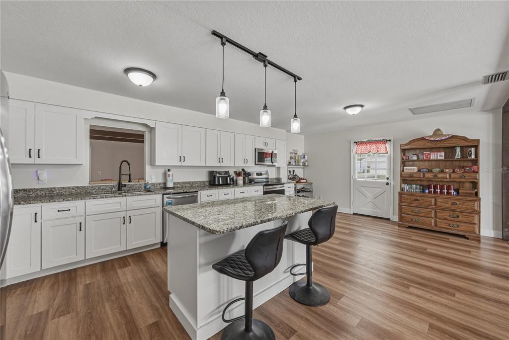 A kitchen with white cabinets, granite countertops, a central island, and wood-look flooring — 609 W PIPKIN ROAD, LAKELAND, FL