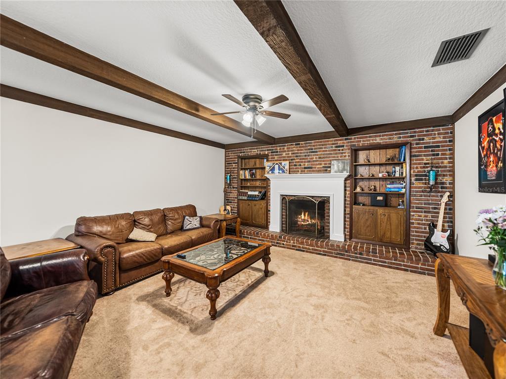 A living room features a brick fireplace, built-in shelving, exposed ceiling beams, and leather furniture — 609 W PIPKIN ROAD, LAKELAND, FL