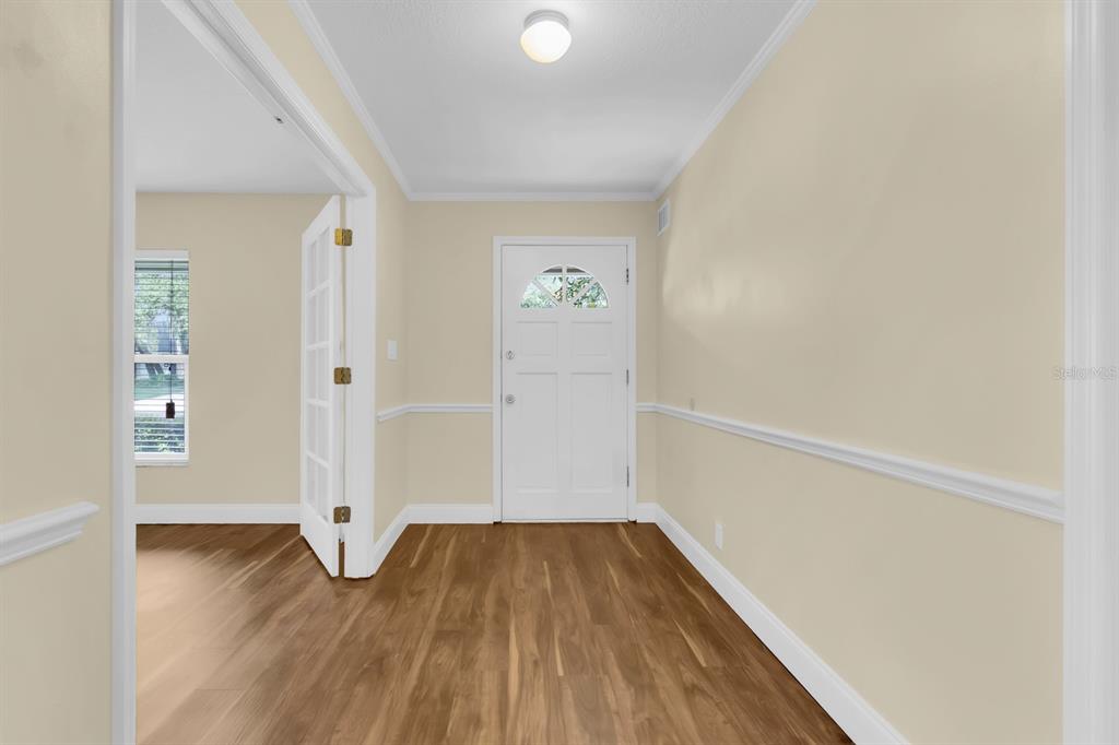 An entryway with light-colored walls, white trim, and wood-look flooring leads to a front door — 215 PALMETTO CONCOURSE, LONGWOOD, FL