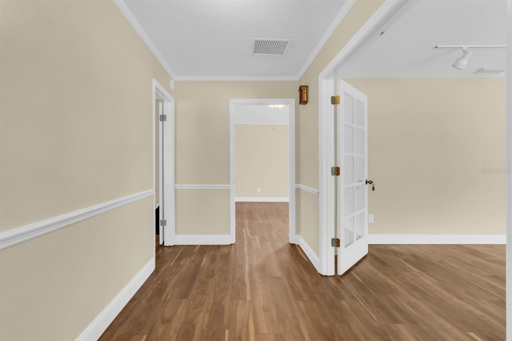 A hallway with wood-look flooring leads to an open doorway and a room with French doors — 215 PALMETTO CONCOURSE, LONGWOOD, FL