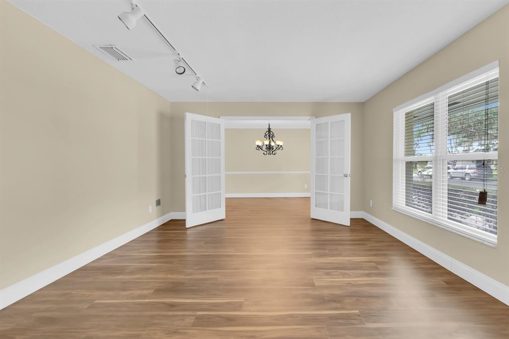 A room with wood-look flooring and French doors opening into a dining area with a chandelier — 215 PALMETTO CONCOURSE, LONGWOOD, FL