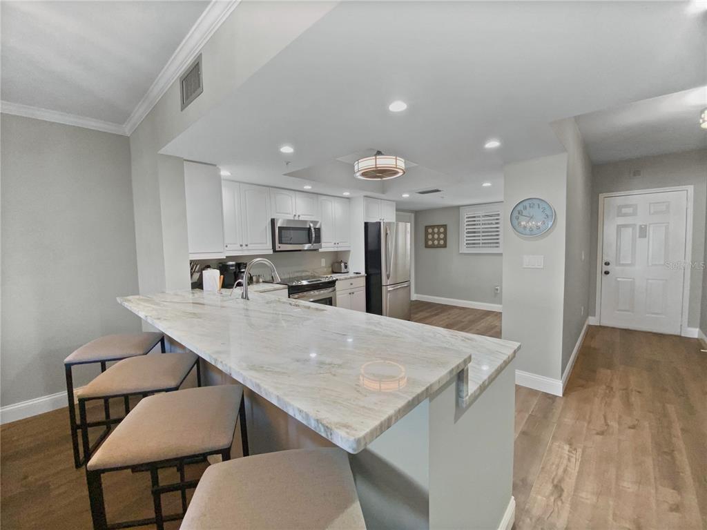 A kitchen features a marble-topped island with bar stools, white cabinetry, and stainless steel appliances — 1445 GULF OF MEXICO DRIVE UNIT 305, LONGBOAT KEY, FL