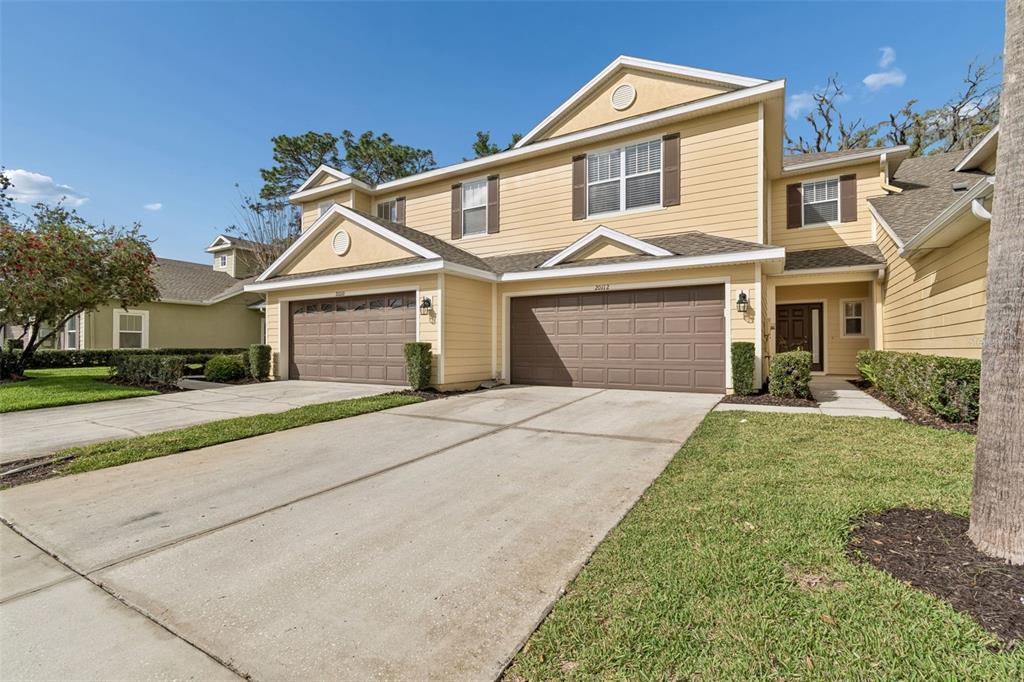 A two-story duplex with yellow siding, brown garage doors, and a concrete driveway — 20112 INDIAN ROSEWOOD DRIVE, TAMPA, FL