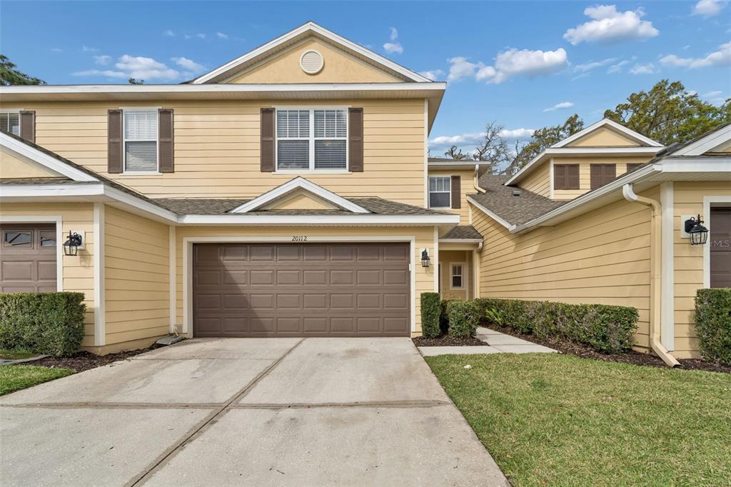 A two-story yellow townhouse with a brown garage door and a concrete driveway — 20112 INDIAN ROSEWOOD DRIVE, TAMPA, FL