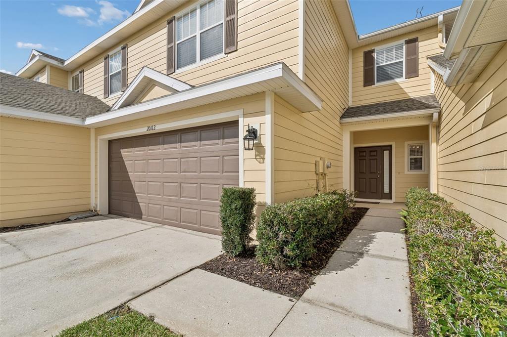 A two-story house with yellow siding, a brown garage door, and a front walkway — 20112 INDIAN ROSEWOOD DRIVE, TAMPA, FL
