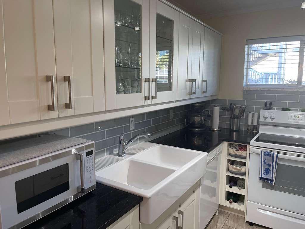 A kitchen features white cabinets, a farmhouse sink, black countertops, and gray subway tile backsplash — 2566 S Garden Drive # 108, Lake Worth FL 33461, LAKE WORTH, FL