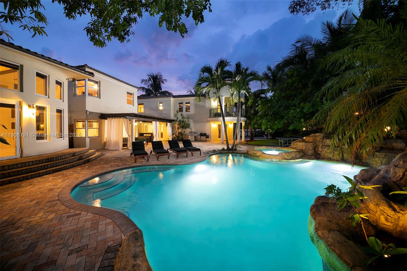 A backyard features a swimming pool with a rock waterfall, a hot tub, and patio furniture — 1051 NE 89th St, Miami FL 33138, MIAMI, FL
