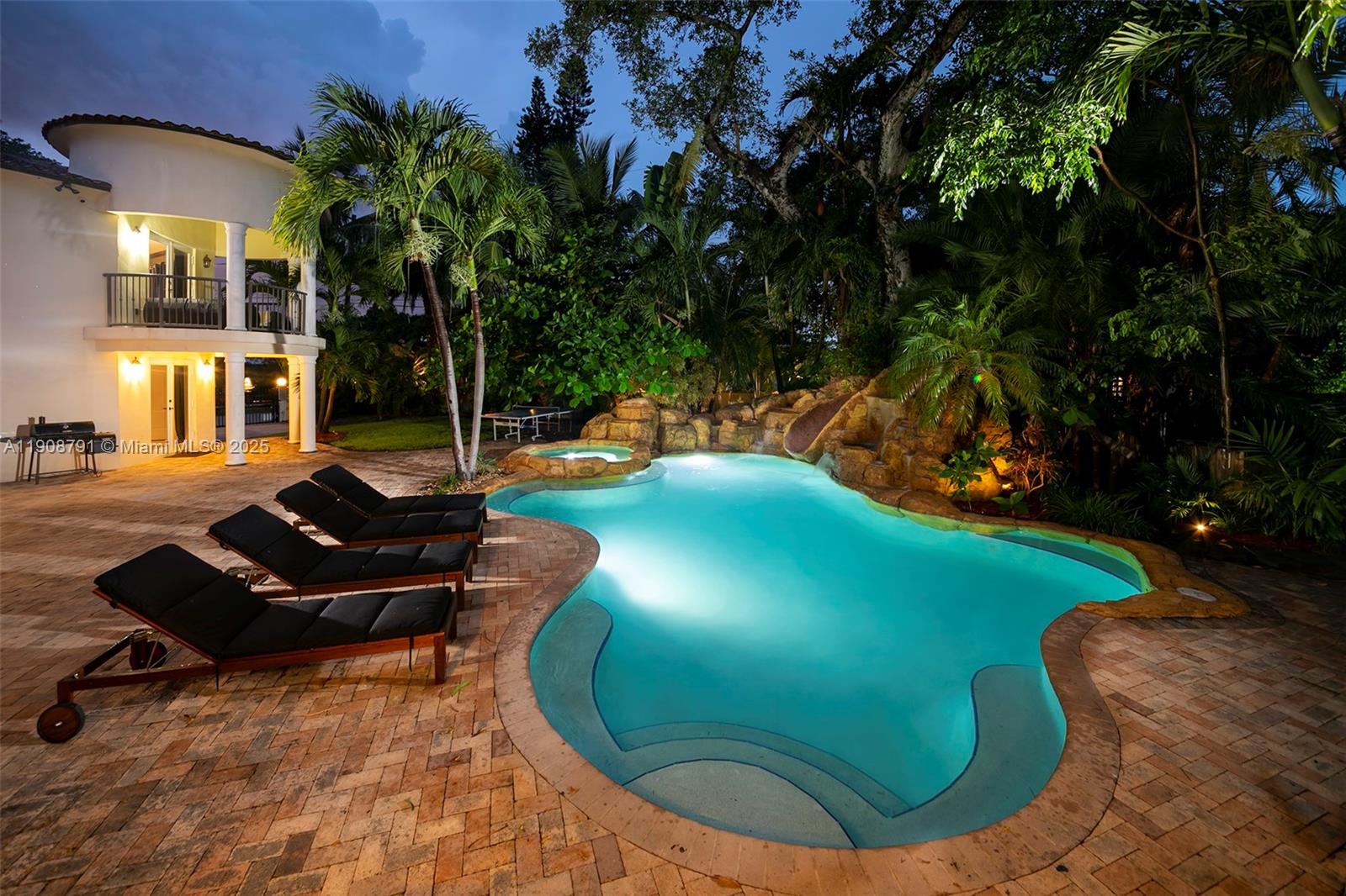 A swimming pool with a rock waterfall and lounge chairs sits on a brick patio — 1051 NE 89th St, Miami FL 33138, MIAMI, FL