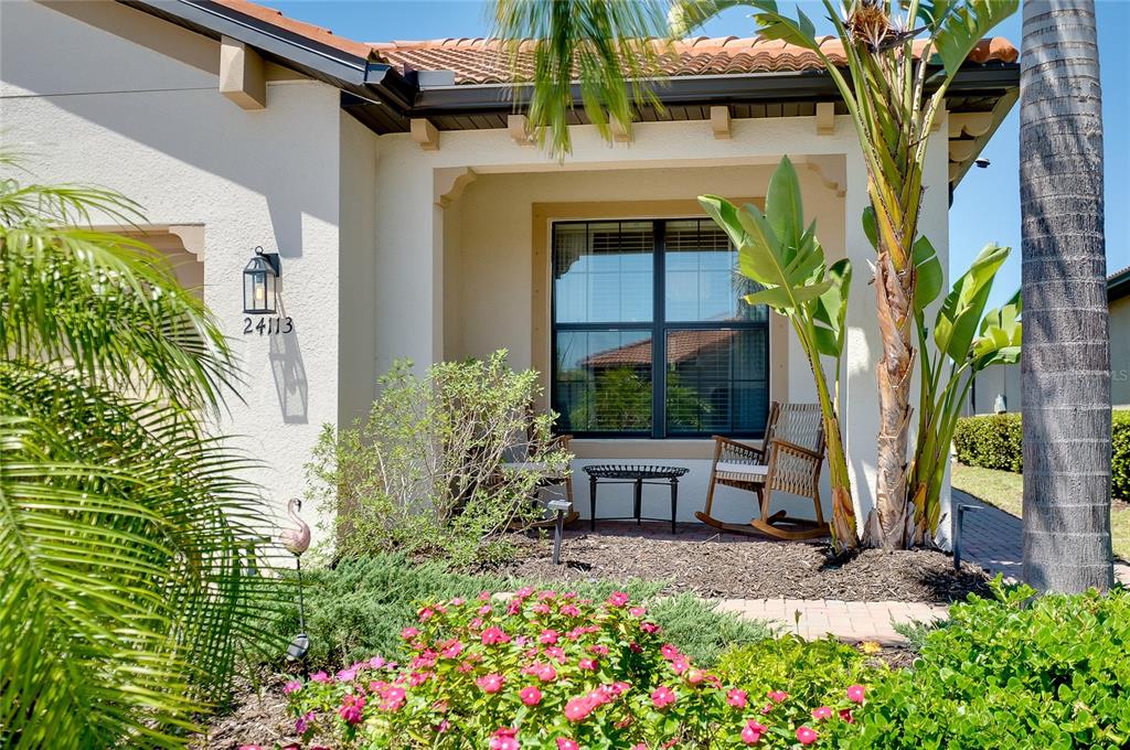 A covered front porch features two rocking chairs, a small table, and landscaping with flowers — 24113 SPARTINA DRIVE, VENICE, FL