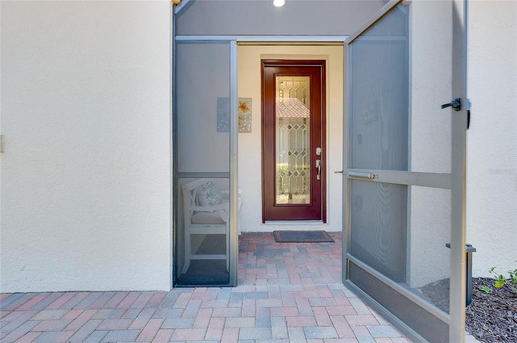 A brick-paved entryway features a dark red front door with a decorative glass insert — 24113 SPARTINA DRIVE, VENICE, FL