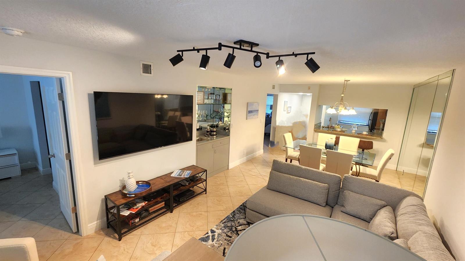A living room features a wall-mounted television, a media console, and a sectional sofa — 600 Egret Circle # 7103, Delray Beach FL 33444, DELRAY BEACH, FL