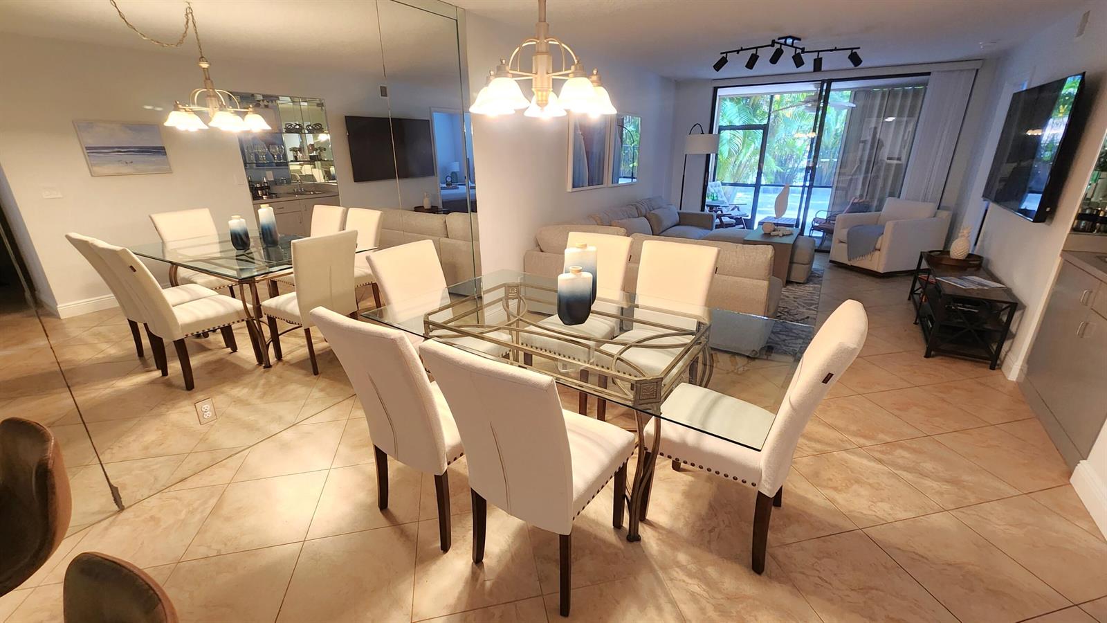 A dining area with a glass table and white chairs sits before a living room — 600 Egret Circle # 7103, Delray Beach FL 33444, DELRAY BEACH, FL