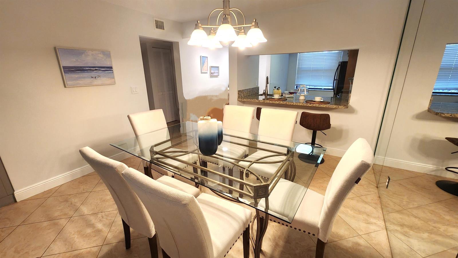 A dining room features a glass-topped table, six upholstered chairs, and a chandelier — 600 Egret Circle # 7103, Delray Beach FL 33444, DELRAY BEACH, FL
