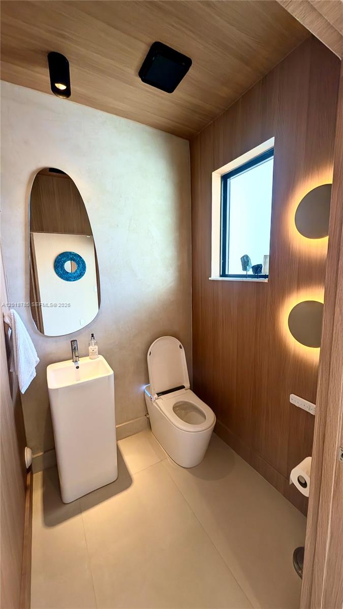 A modern bathroom features a pedestal sink, a toilet, and wood-paneled walls with accent lighting — 20865 NE 7th Ct, Miami FL 33179, MIAMI, FL