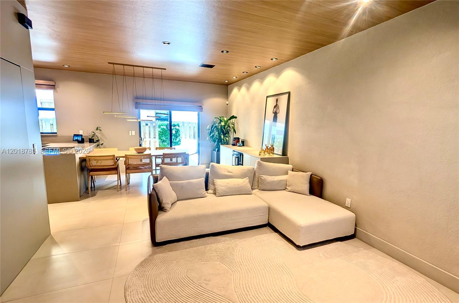 A modern living room features a beige sectional sofa, wood-paneled ceiling, and an adjacent dining area — 20865 NE 7th Ct, Miami FL 33179, MIAMI, FL