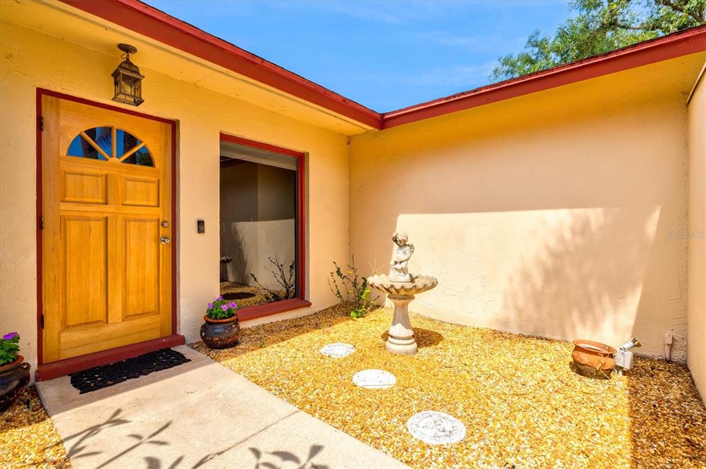 A front entryway features a wooden door, a stone fountain, and a gravel courtyard — 6533 BOWLINE DRIVE, SARASOTA, FL