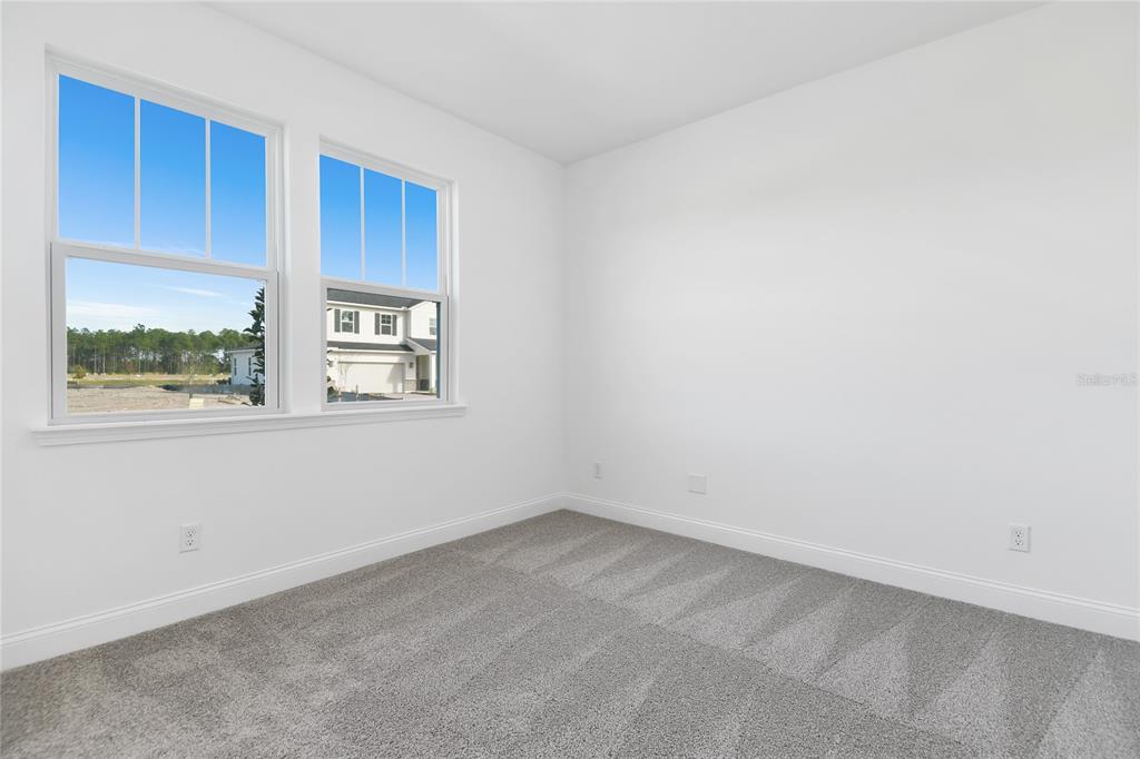 An empty bedroom with white walls, gray carpet, and two windows overlooking a construction site — 188 ENCLAVE AVENUE, PALM COAST, FL