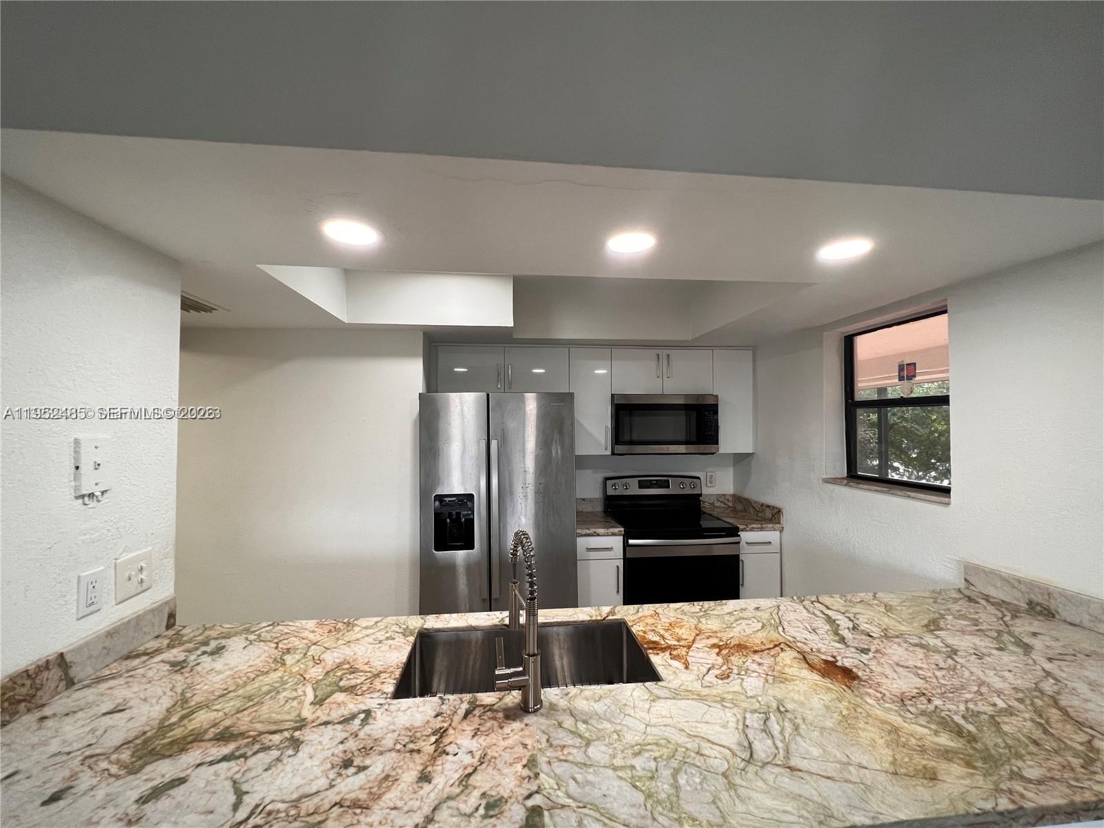 A kitchen features stainless steel appliances, white cabinets, and a patterned stone countertop — 16220 NW 2nd Ave # 511, Miami FL 33169, MIAMI, FL