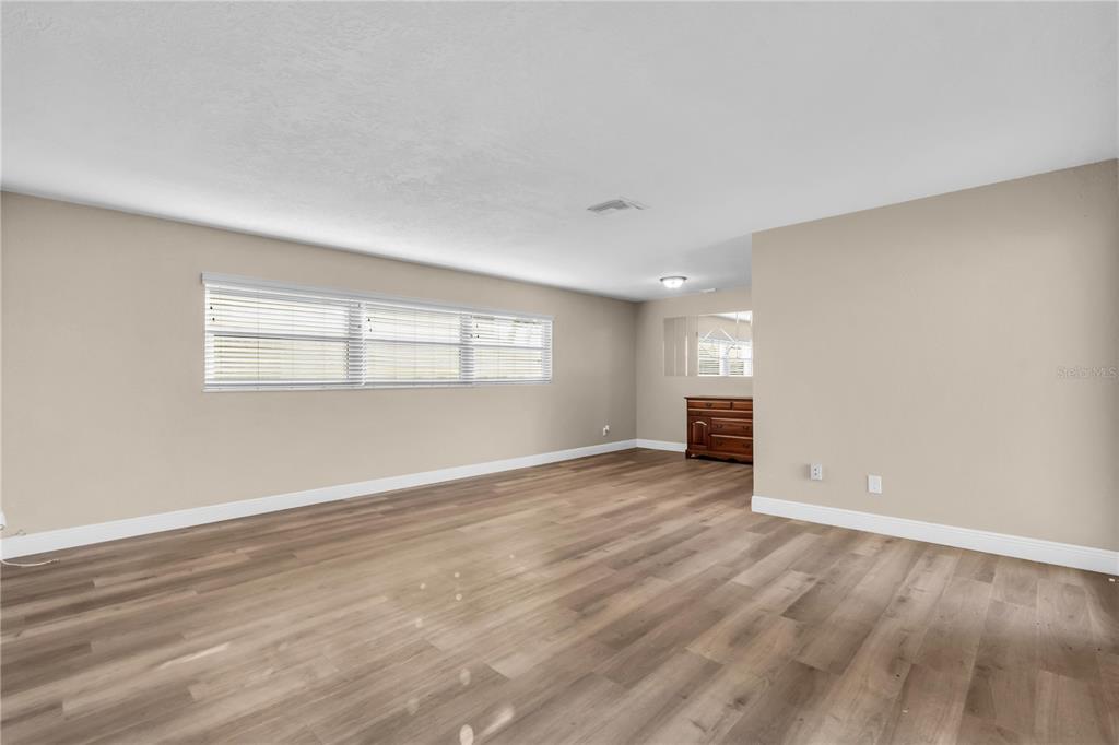 An empty room with light-colored walls, wood-look flooring, and a large window with blinds — 6860 PARK STREET S, SOUTH PASADENA, FL